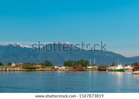 Beautiful bay with tourist and fishing boats and a view of Mount Olympus in the background. Katerini Paralia beach, Pieria, Greece. Colorful greek picture with sea, sky and mountains. Travel concept.