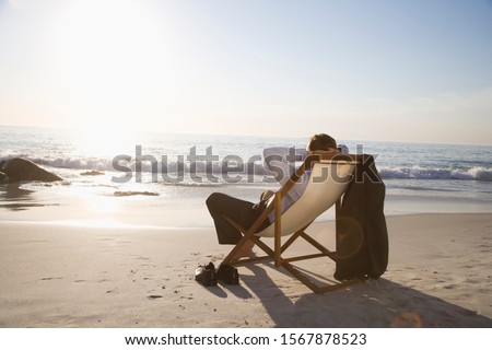 Businessman sitting in deck chair at beach Royalty-Free Stock Photo #1567878523