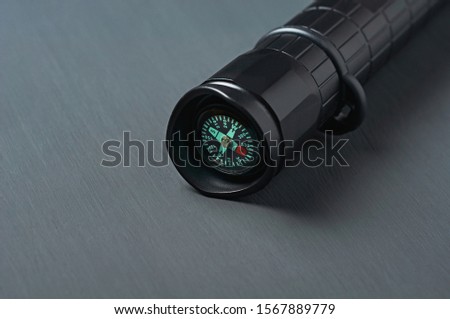 One black tactical flashlight with compass for survival lies on dark concrete table. Space for text. Close-up