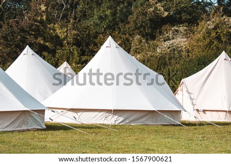 Light creme canvas waterproof tent in a green field on a nice and hot summer day. Blue Clouds, green grass, Child festival tent. Royalty-Free Stock Photo #1567900621