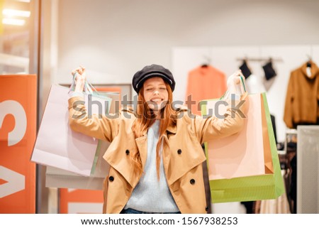 shopping concept. young caucasian shopaholic with red hair raised hands up, holdig paper bags full of new trendy clothes dresses