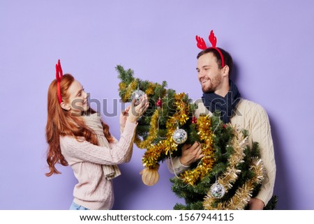 Pleasant pretty man together with redhead woman, dressed in warm knitted clothes, prepare everything for Merry Christmas, young lady touching bauble on beautiful fir