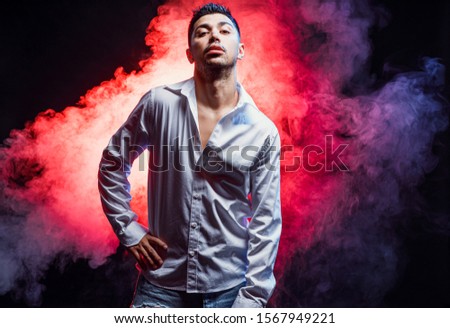 brunette male dancer posing at camera, wearing white shirt, looking at camera isolated over colorful smoky background