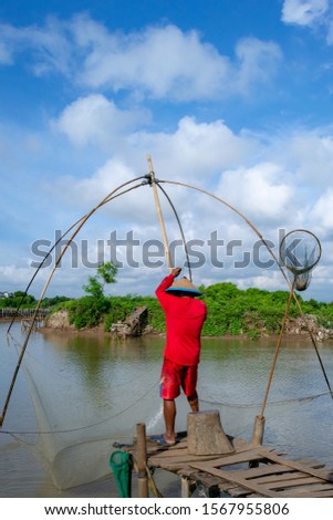 A fisherman is catching fish with fishing nets during the day under a cloudy sky
