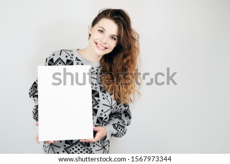 Happy european girl holding a blank vertical canvas in her hands. Empty frame for text or photo. Young woman with mockup poster on grey background.