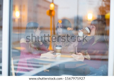 Mother and daughters sitting in cafe drinking coffee and taking. have conversation, happy and sad.  Picture through window.