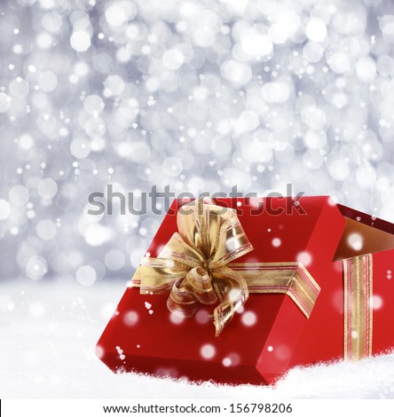 Red Christmas gift box with its lid propped at an angle in front to display the beautiful shiny metallic gold ribbon with falling winter snowflakes and copyspace for your greeting or wishes