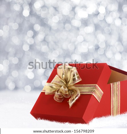 Colourful red Christmas gift decorated with a gold ribbon and bow in winter snow with a bokeh of falling snowflakes and copyspace for your seasonal greeting