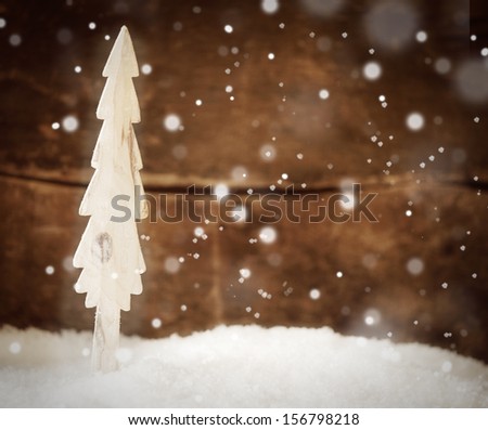 Pretty Christmas card background with a simple wooden Christmas tree standing in snow during a snowfall against a rustuc wooden wall with copypsace for your greeting