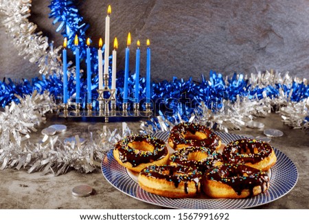 Jewish holiday Hanukkah background. Menorah with burning candles and sweet donuts with chocolate and sprinkle on the top.