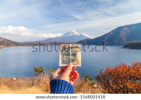 The view of Lake Motoko with a woman's hand holding 1000 yen bank. One of the 5 lakes around Mount Fuji, in the bright blue sky. Japan's landmark, Japan, Fuji san Royalty-Free Stock Photo #1568001418