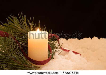 lit white candle and  pine needles in snow. Black Christmas Background with holiday theme.
