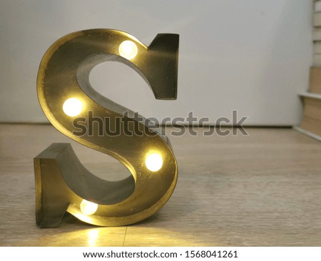 Electric light up lamp alphabet in hard font. Letter S on wood floor. 