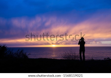 A woman taking photo of the sunset in the ocean. 