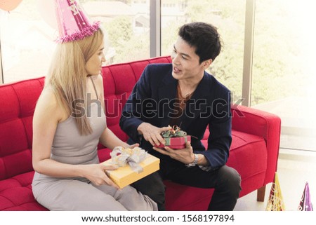 Young happy Asian couple in love have fun on the red sofa and holding a surprise gift present box on new years eve party. or valentines day.