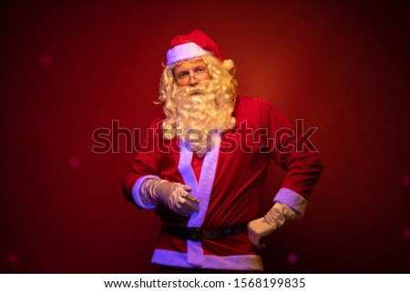 Male actor dressed as Santa Claus posing on a dark red background.