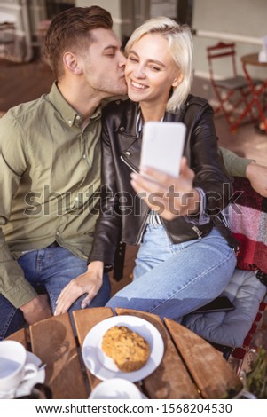 Handsome young man kissing his pretty girlfriend taking a selfie