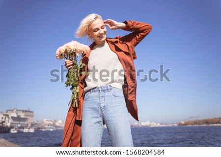 Pretty young lady holding flower bunch in one hand and touching her hair with another