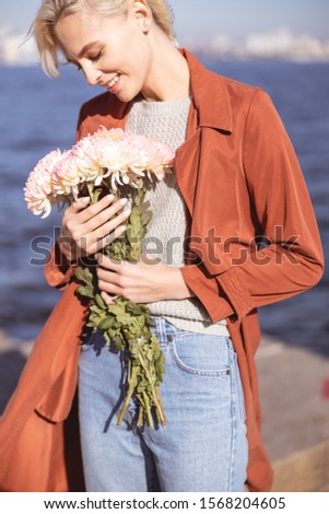 Beautiful young lady holding close her flower bouquet and smiling