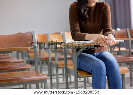 Asian female student wearing a brown shirt is intending to study as the teacher has taught in the classroom.