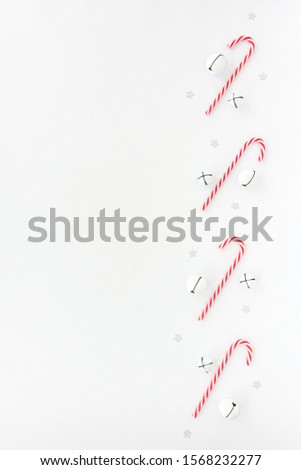 Christmas background with white jingle bells, candy canes and silver star confetti isolated on white. Top view.