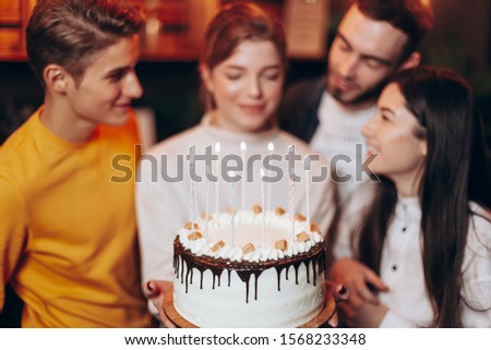 attractive girl blows out the candles on the cake and makes a wish near the best friends who came to congratulate her on her birthday
