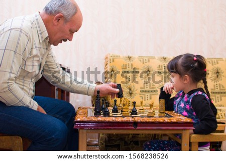 cute girl playing chess at home with her grandfather
