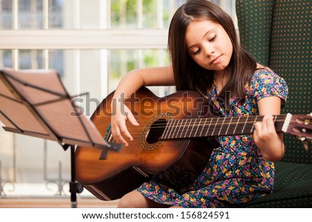 Pretty little girl practicing some new sound on a guitar at home Royalty-Free Stock Photo #156824591