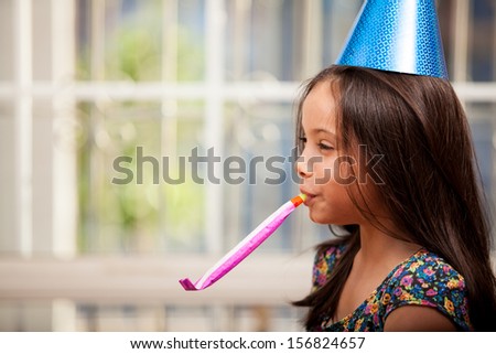 Happy little girl wearing a party hat celebrating her birthday and blowing a noisemaker