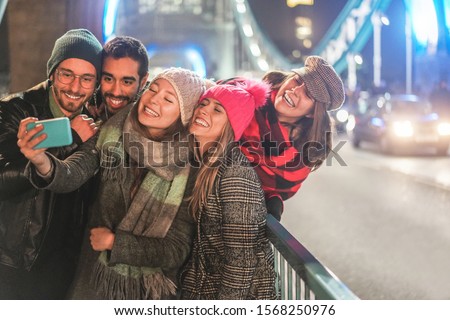 Happy millennial friends taking slow motion videos on city bridge at night time - Young people having fun with new trends technology - Travel and friendship concept - Focus on two center girls faces