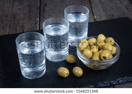 Vodka shot and green olives on dark table.