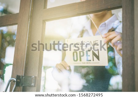 Store owner turning open sign broad through the door glass and ready to service. man with open banner at cafe or restaurant window.