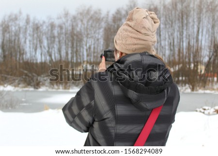  photo of a girl with a camera.she takes pictures of the winter landscape.it's cold outside.woman photographs the river with ice and forest.trees without leaves.everywhere lies white snow.