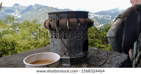 A cup of tea kept on a table along with a heater with a view of mountains in the background.