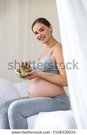 Happy young expectant mother sitting on bed with food stock photo