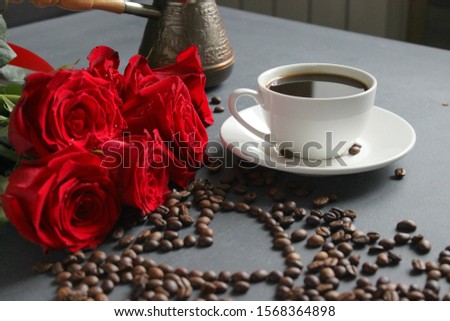 A white Cup of coffee and a bouquet of red roses on the table. Scattered coffee beans in the shape of a heart. Love, love of coffee, nice Breakfast. Copy space. cup, coffee beans, flavor 