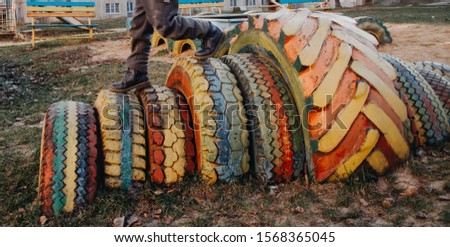 The Playground is made of old car tires. Tires, wheels painted with colorful paints. The child runs on the tires dug into the ground. Fun game.