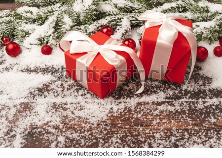 Presents on wooden background with fir tree branches and red baubles powdered with snow