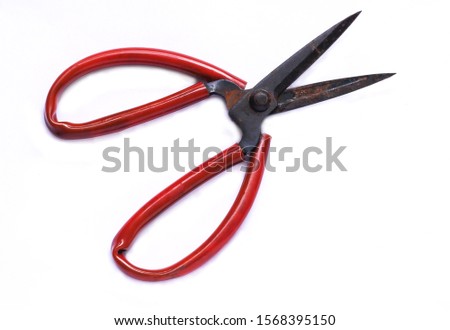 Old rusty scissors with red rubber handle on white background