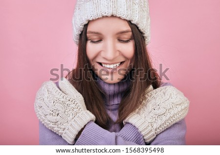 Fascinating lady with closed eyes, dark hair, in a knitted sweater and crossed her arms over her chest. She smiles slightly. Portrait on pink background. The atmosphere of comfort.