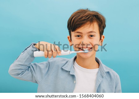 Mixed race little boy cleaning teeth with sonic toothbrush on blue background. Perfect removing plaque with cool toothbrush