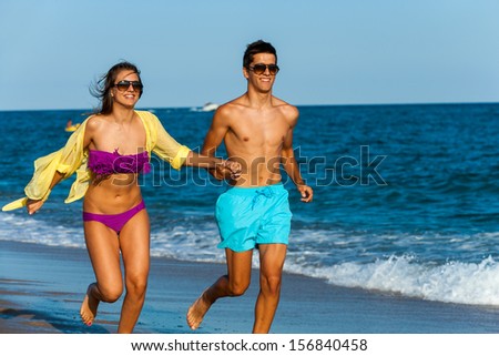Teen couple holding hands while running along beach.