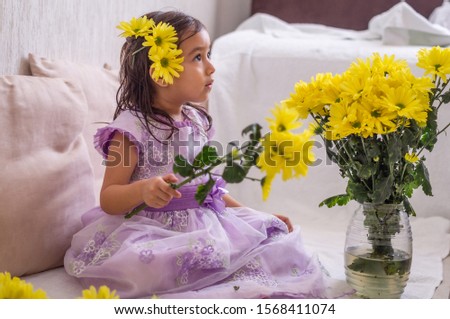Little girl with yellow flowers in her hair and bouquet in hands, serious intense look