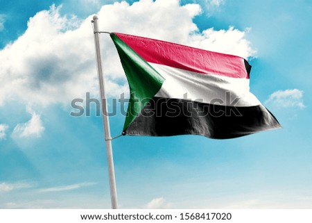 Waving Flag of Sudan in Blue Sky. Sudan Flag on pole for Independence day. The symbol of the state on wavy cotton fabric.