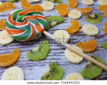 
close-up of a large round fruit lollipop on a background of slices of banana, kiwi, tangerine / orange