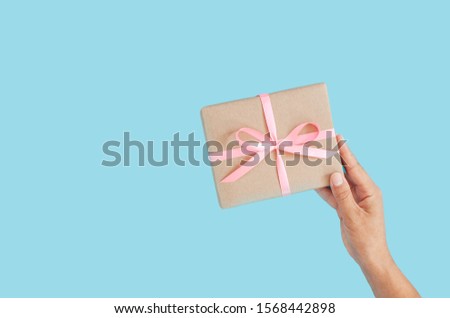 Female hands holding present box or gift box package in craft paper over blue background. Top view, flat lay