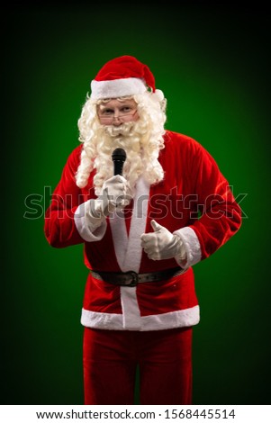 Male actor in a costume of Santa Claus holds a microphone in his hands, sings and poses on a dark red background