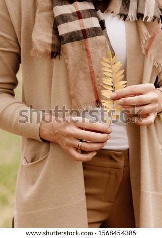 yellow leaves in hands of woman in beige casual jacket 