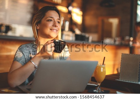 Beautiful young woman enjoying her first morning coffee in a coffee shop looking out the window