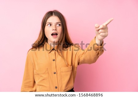 Ukrainian teenager girl over isolated pink background pointing away